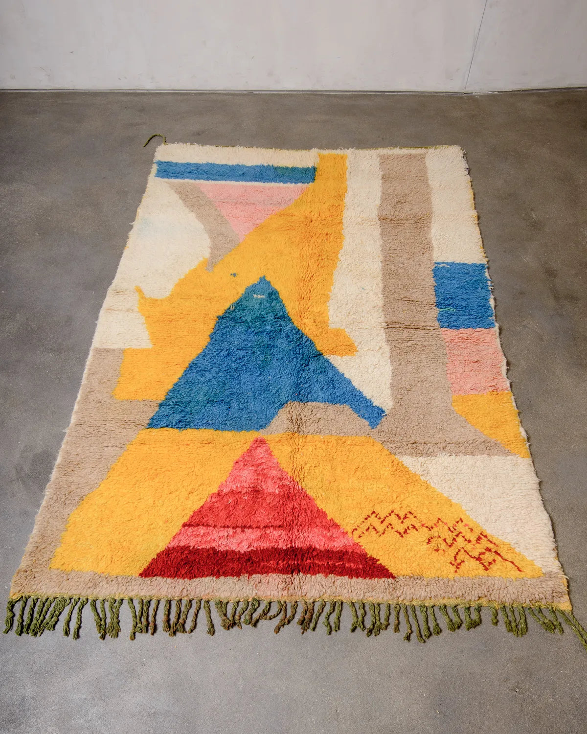 Berberlin vintage wool Boujad rug featuring saffron yellow, blue and sand, laying on concrete floor.